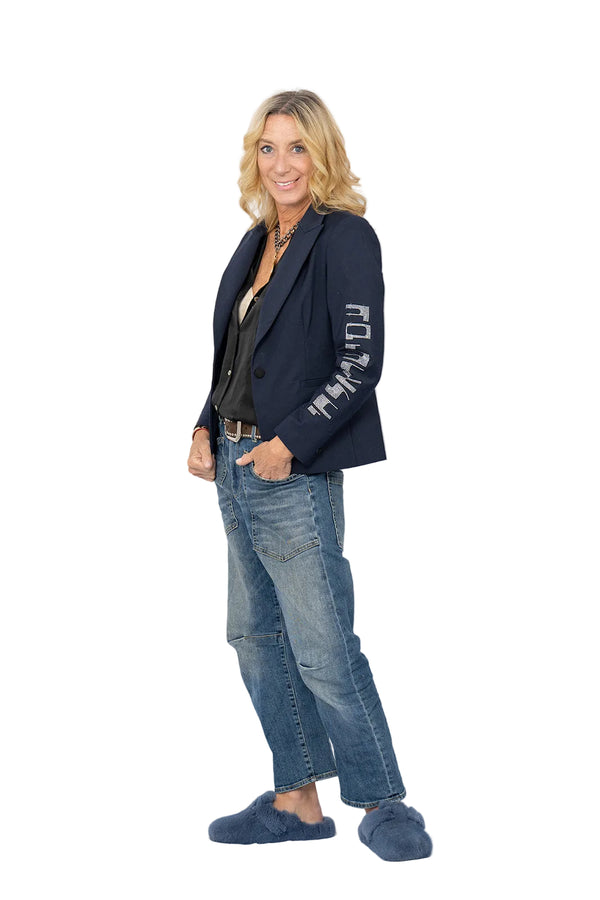 Woman wearing a navy blazer with text, blue jeans, and blue shoes on a white background