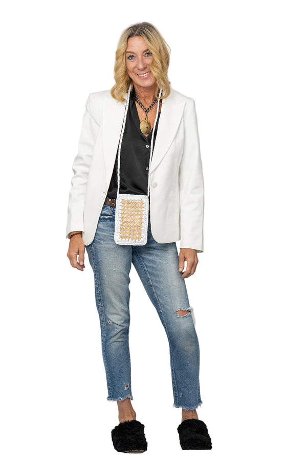 Woman wearing a white blazer, black top, blue jeans, and black shoes on a white background