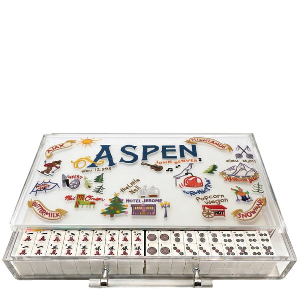 Aspen-themed domino game set in a clear plastic case with illustrated winter and mountain motifs on the top cover, shown open with domino tiles and pips visible against a white background.