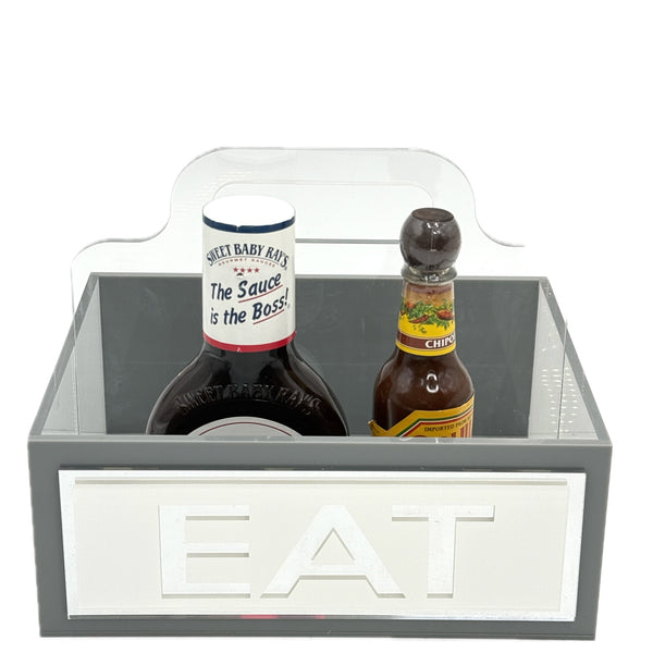 Gray acrylic EAT caddy with white lettering and condiment bottles inside.