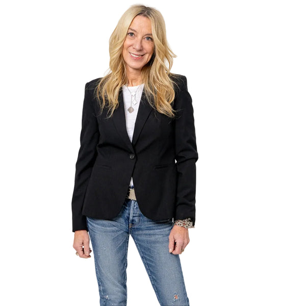 Woman wearing a black blazer over a white top with blue jeans.
