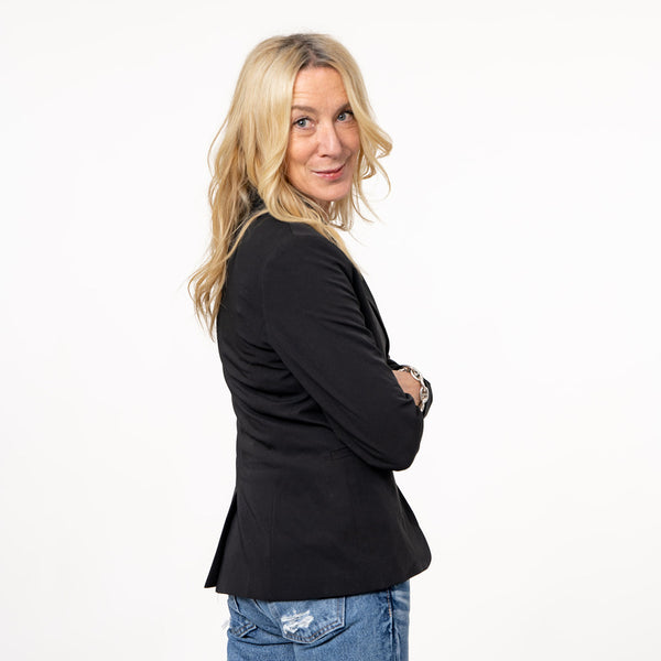 Side view of a woman wearing a black blazer and blue jeans.