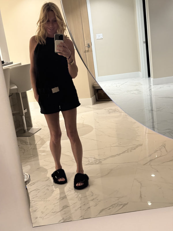 Woman taking a mirror photo while wearing a black sleeveless dress and black fur slide sandals.