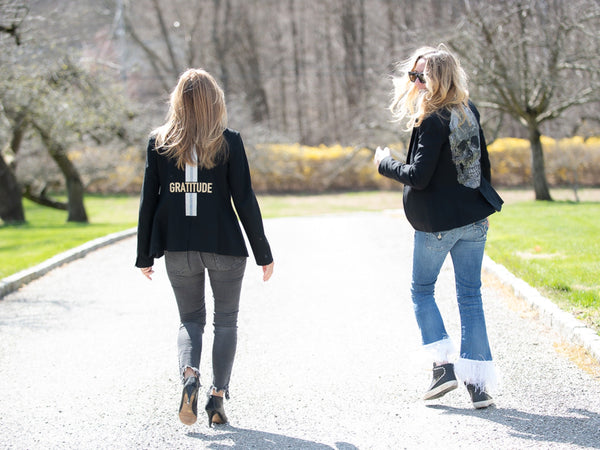 Two women outdoors wearing black blazers with BLESSED lettering and a skull design on their backs.