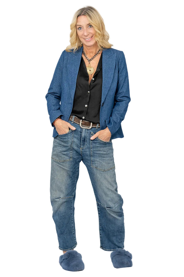 Woman wearing a blue denim blazer with a black blouse, blue jeans and blue slides.