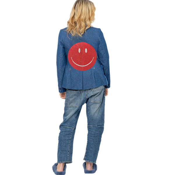 Woman wearing a blue denim blazer with a large red crystal smiley face on the back.