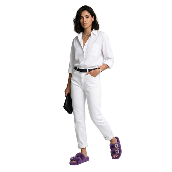 Woman wearing a white shirt and pants with purple sandals in a minimalistic room.