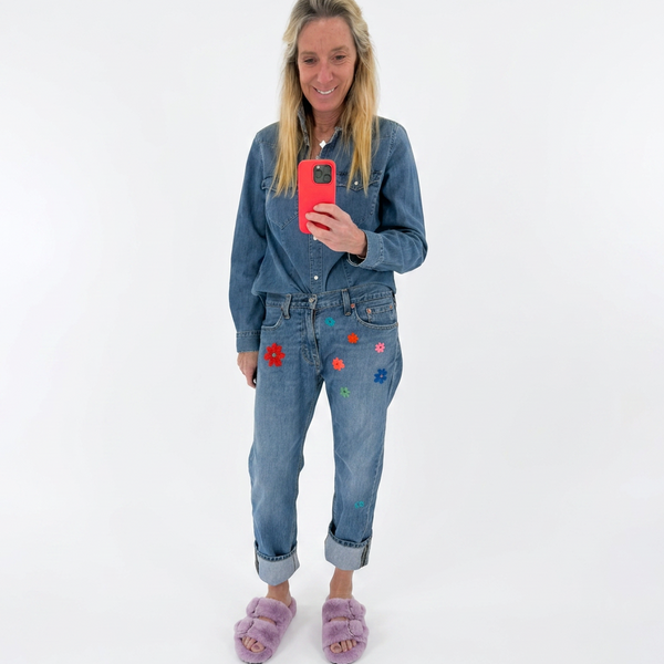Woman wearing blue jeans with floral patches, holding a red phone on a white background