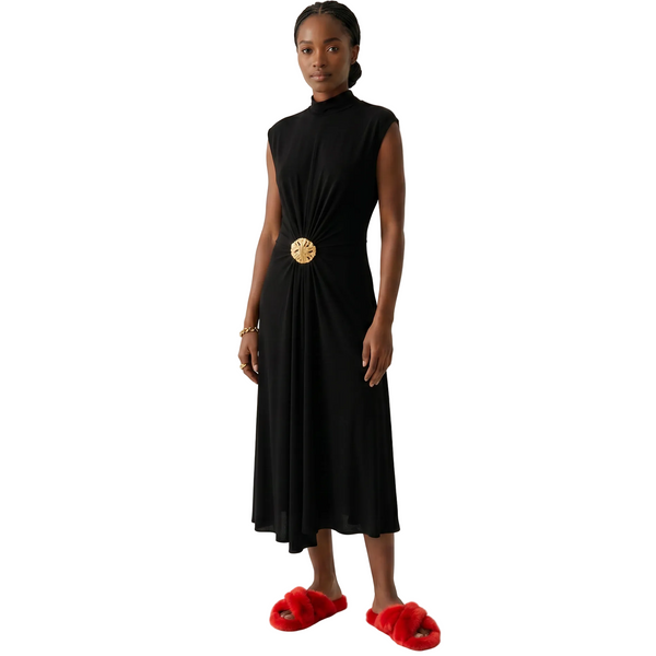 Woman wearing a black dress with a gold belt and red slippers on a white background