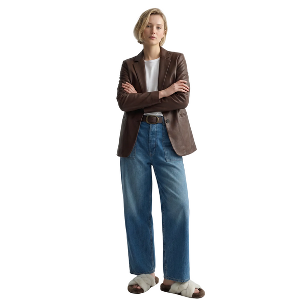 Person wearing a brown blazer, white shirt, blue jeans, and sandals on a light gray background