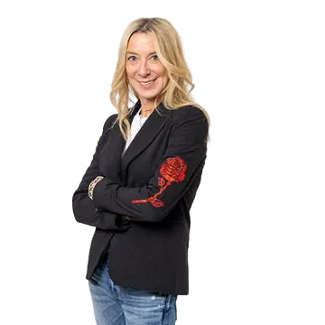 Woman wearing a black blazer with a red rose design on the sleeve and blue jeans, standing with her arms crossed.
