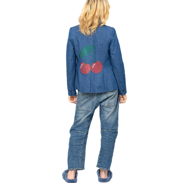 Woman wearing a blue denim blazer with red rhinestone cherries and a green leaf on the back.