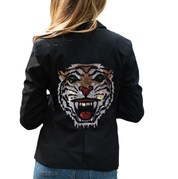 Woman wearing a black blazer with a rhinestone tiger face and green eyes on the back.
