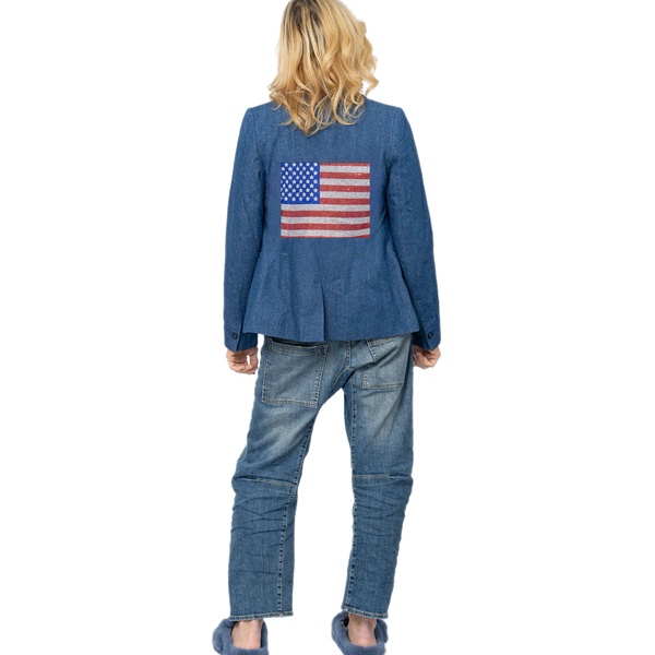 Back view of a woman wearing a blue denim blazer with a rhinestone American flag, blue jeans and blue fur slides.