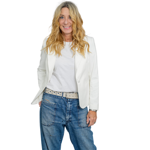Woman wearing a white blazer over a white top with blue jeans.